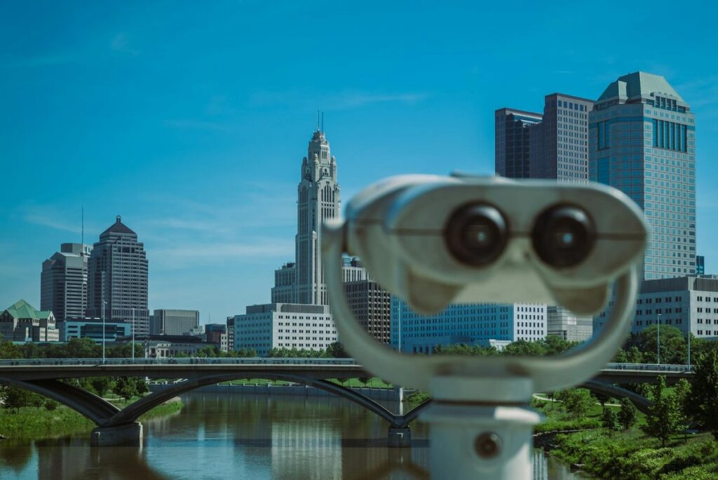 A coin operated telescope focusing on a city skyline with tall buildings and a bridge.