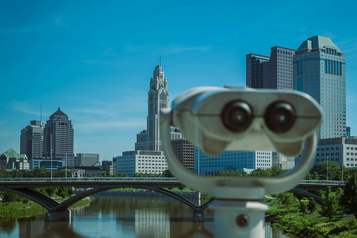 A coin operated telescope focusing on a city skyline with tall buildings and a bridge.