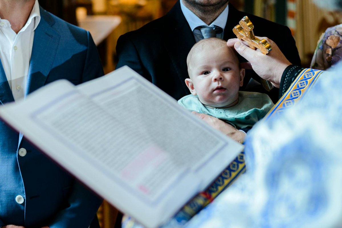 A Romanian baptism ceremony showing a priest blessing a baby with holy cross.