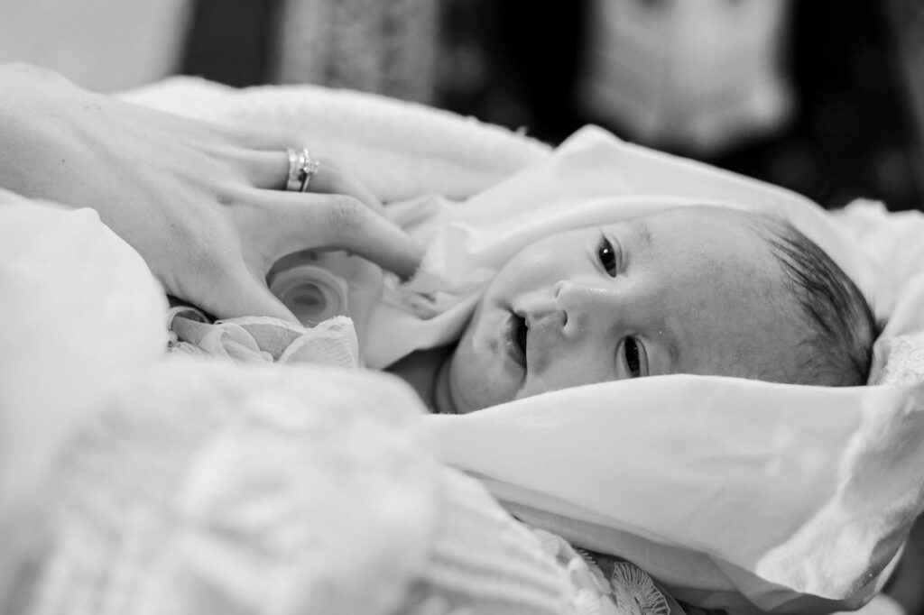 Tender black and white portrait of a newborn wrapped in fabric, touched by a gentle hand.