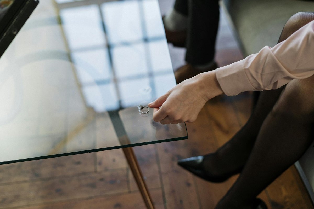Close-up of a woman placing a wedding ring on a glass table, symbolizing relationship changes.