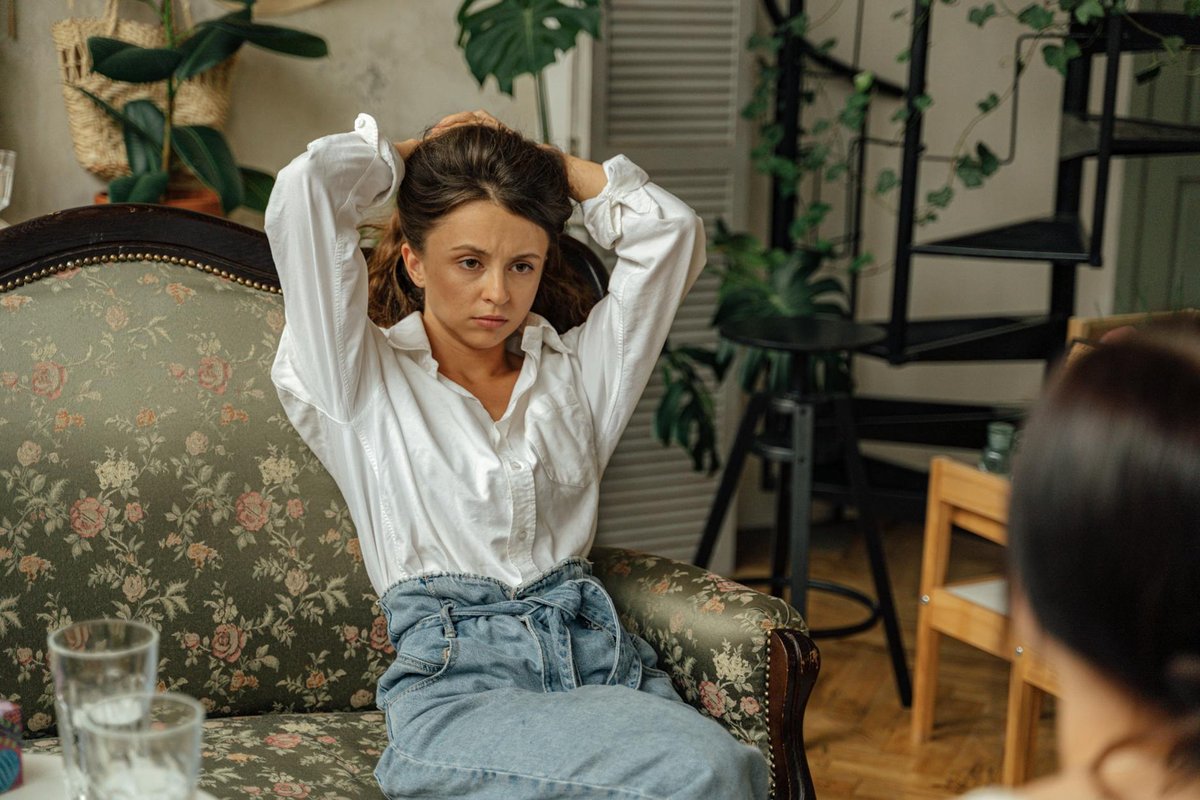 Woman sitting on a floral couch, appearing deep in thought in a cozy living room setting.