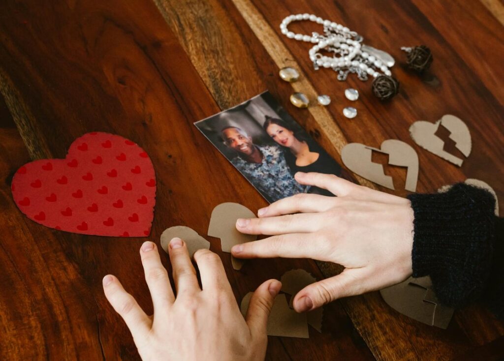 Close-up of hands arranging broken hearts near a couple's photo on a wooden table.