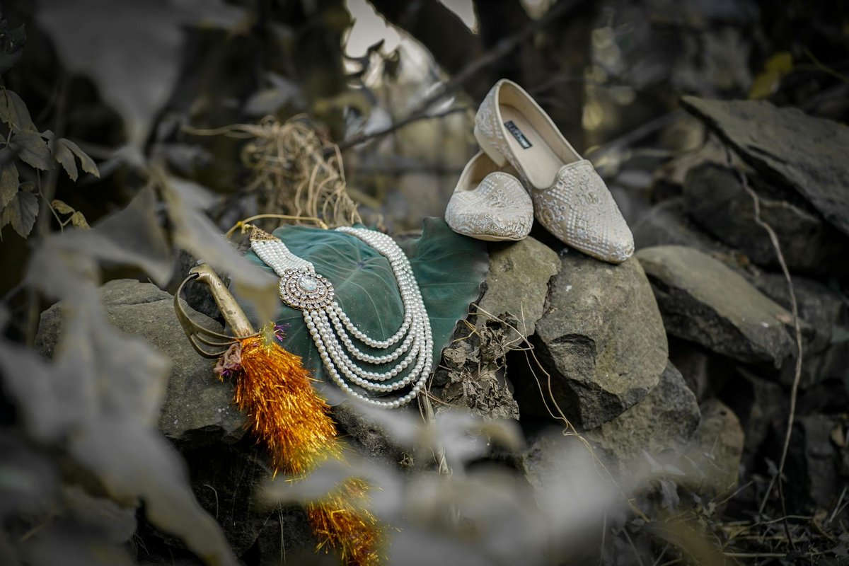 Close-up of bridal jewelry and shoes on natural stones with rustic background.