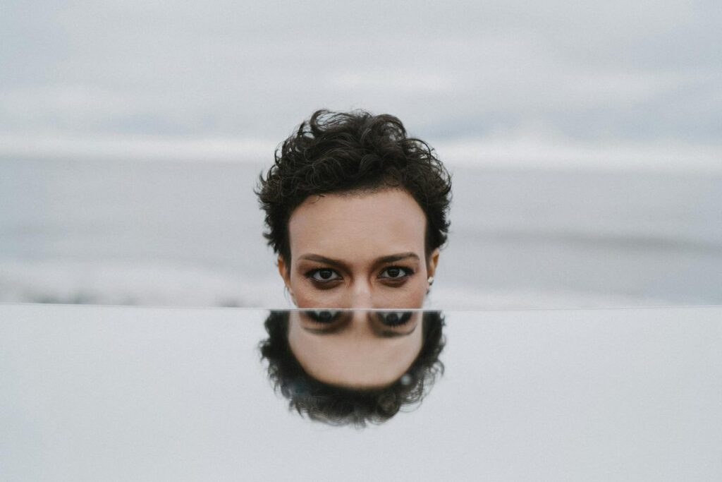 A moody portrait of a person reflected in a mirror with the ocean as a backdrop.