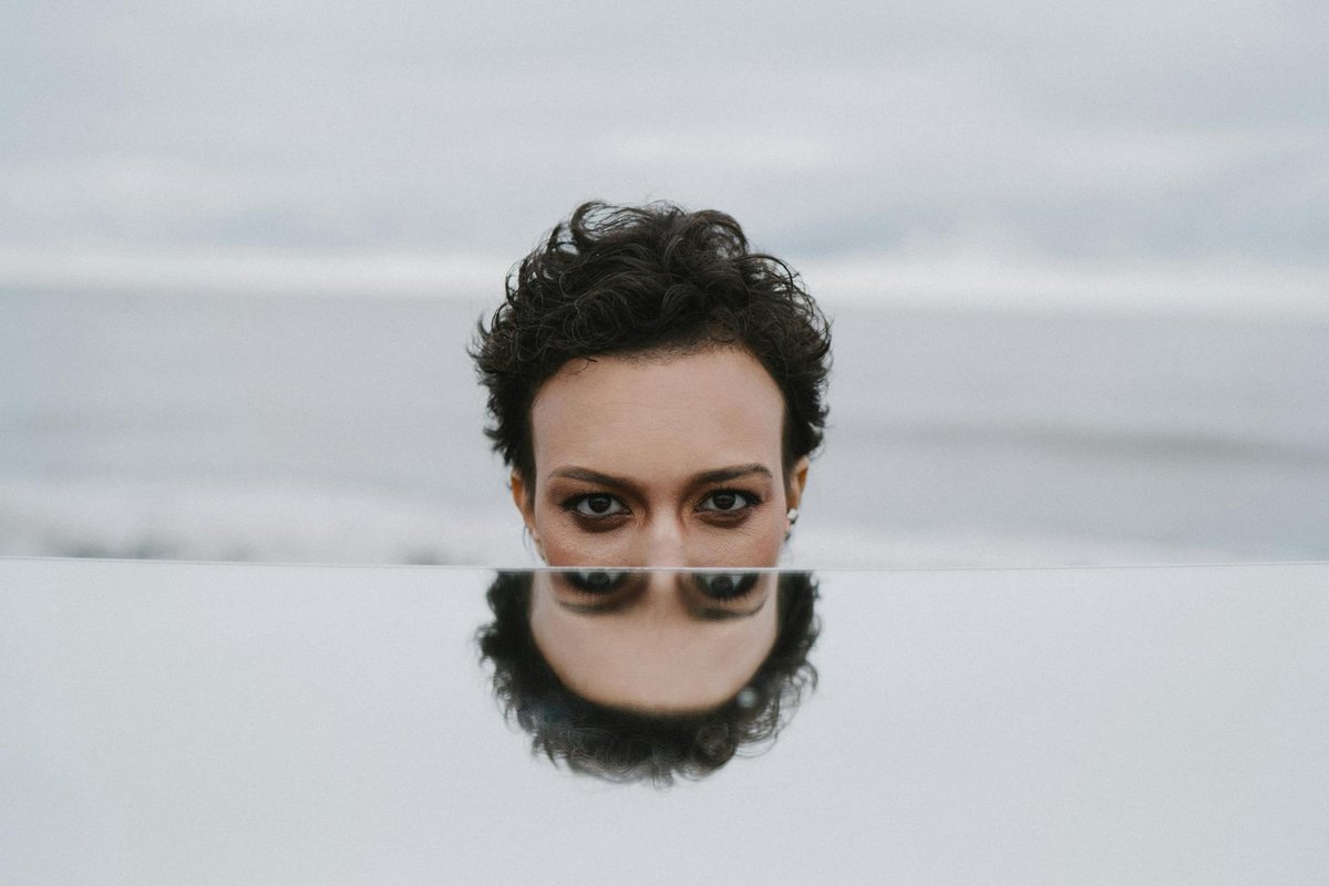 A moody portrait of a person reflected in a mirror with the ocean as a backdrop.