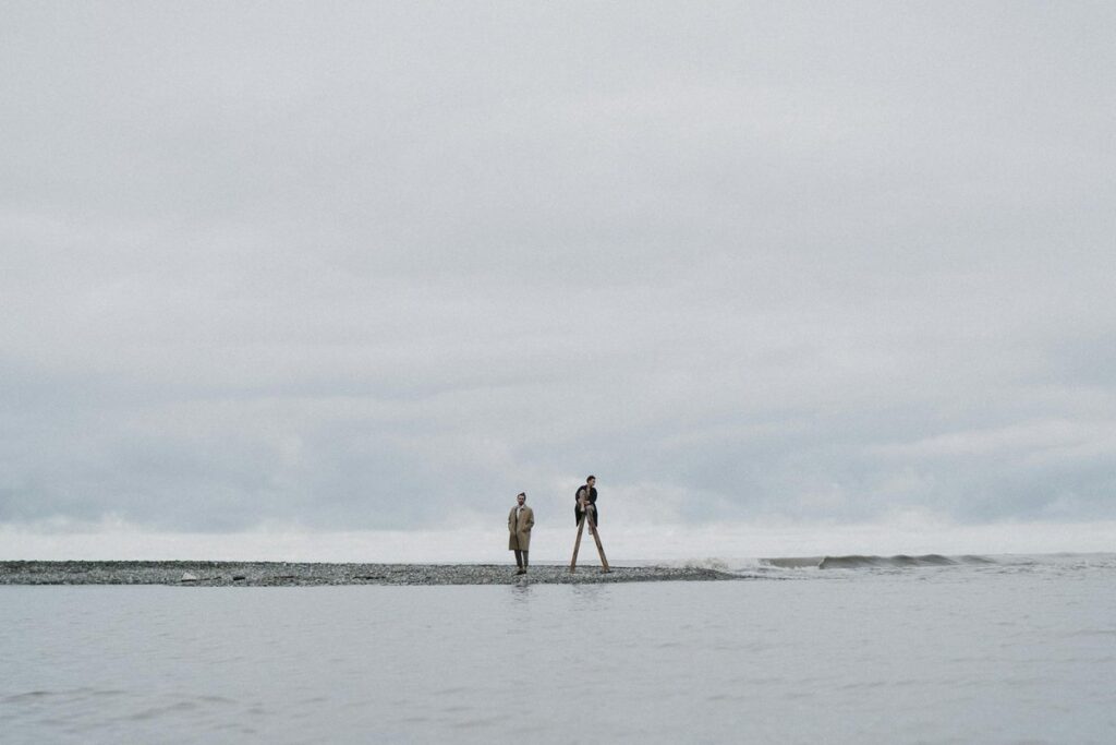 Two individuals walking along a serene, cloudy beachfront, capturing solitude and reflection.