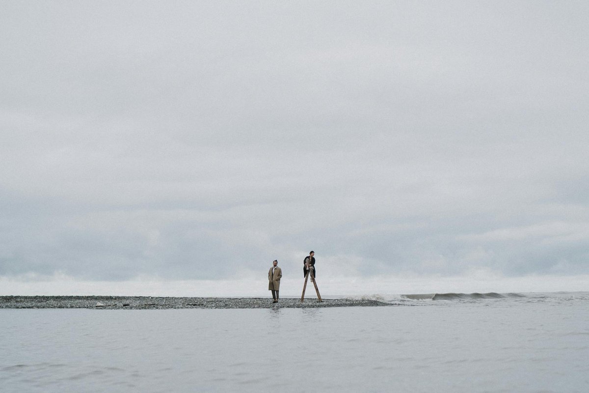 Two individuals walking along a serene, cloudy beachfront, capturing solitude and reflection.