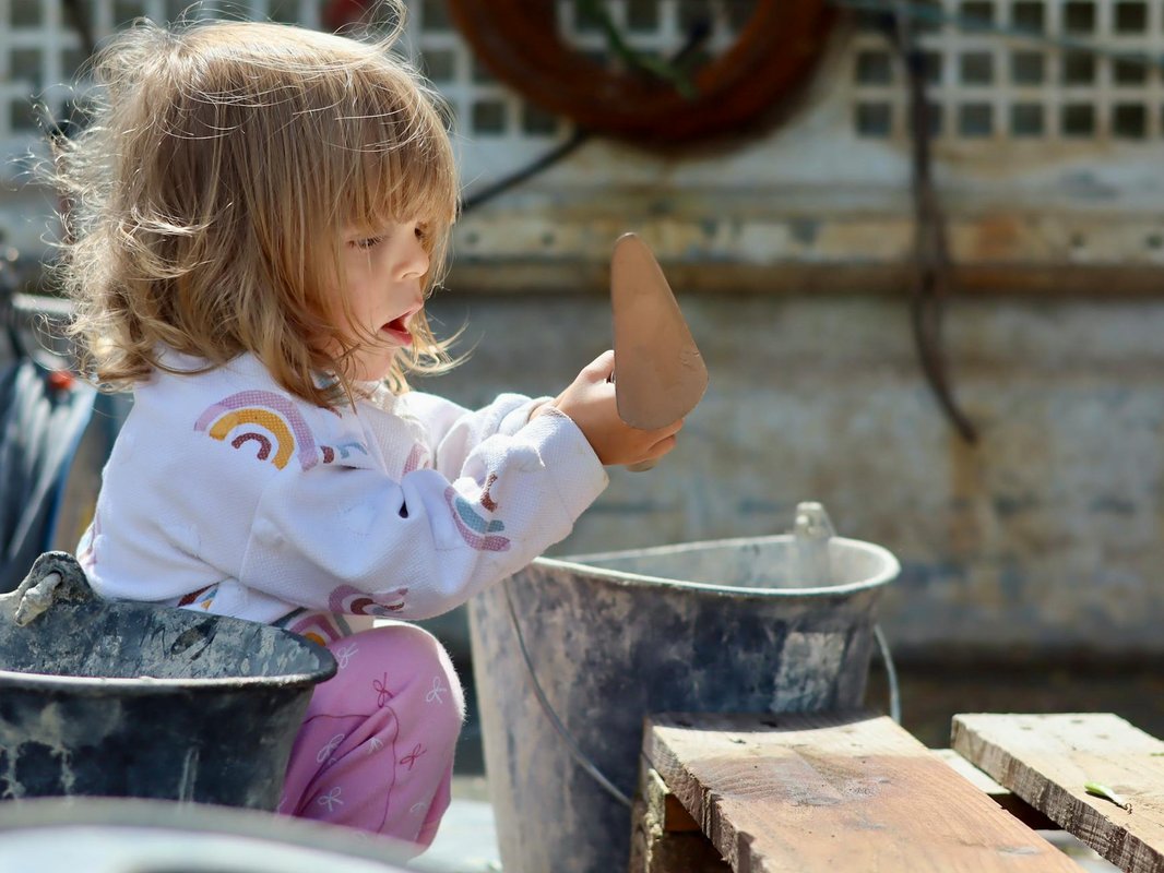 Young child exploring with a plastic shovel in an outdoor building environment.