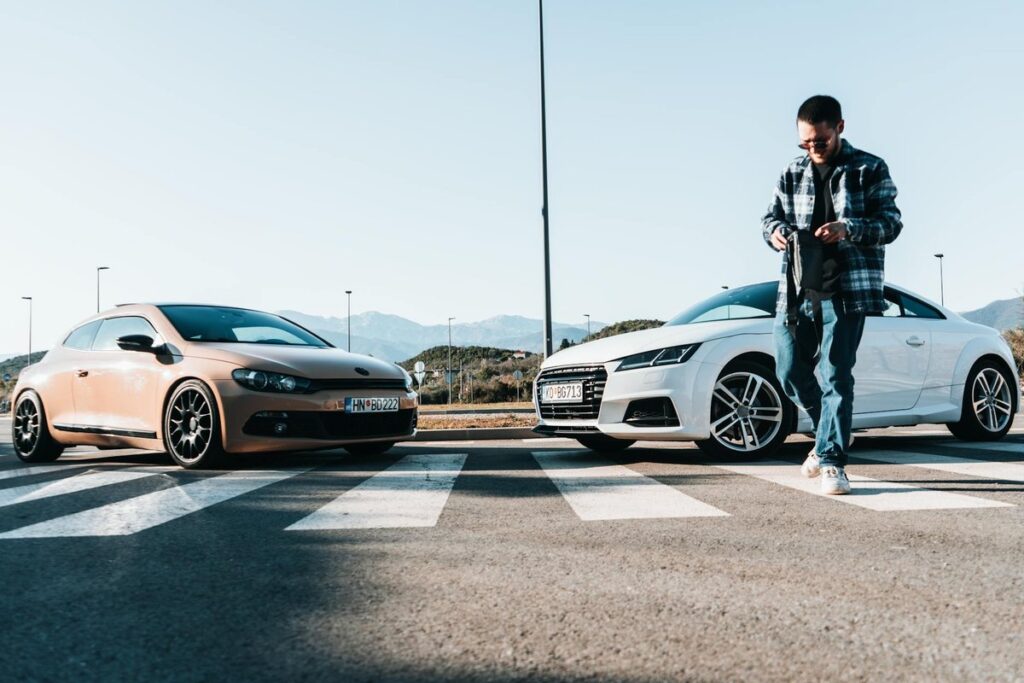Young man standing near two cars on a crosswalk in Tivat, Montenegro during a sunny day.