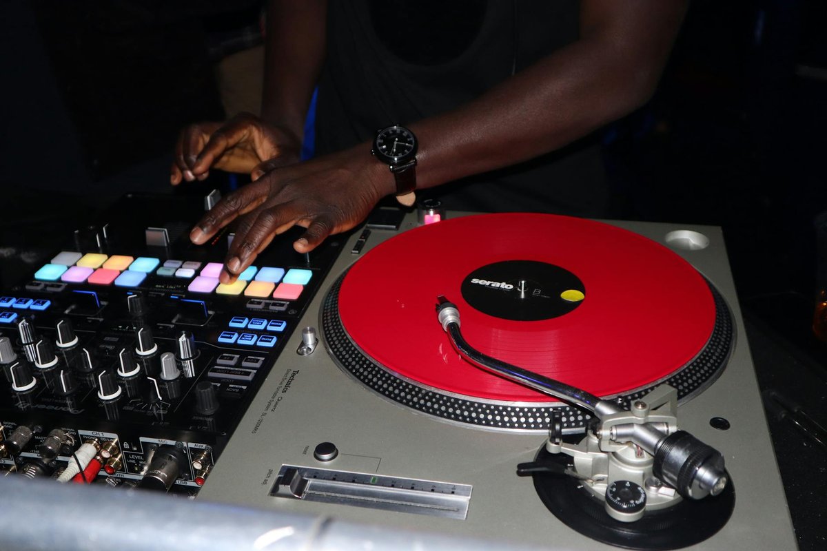 DJ skillfully mixing music on a red vinyl turntable in a dimly lit setting.