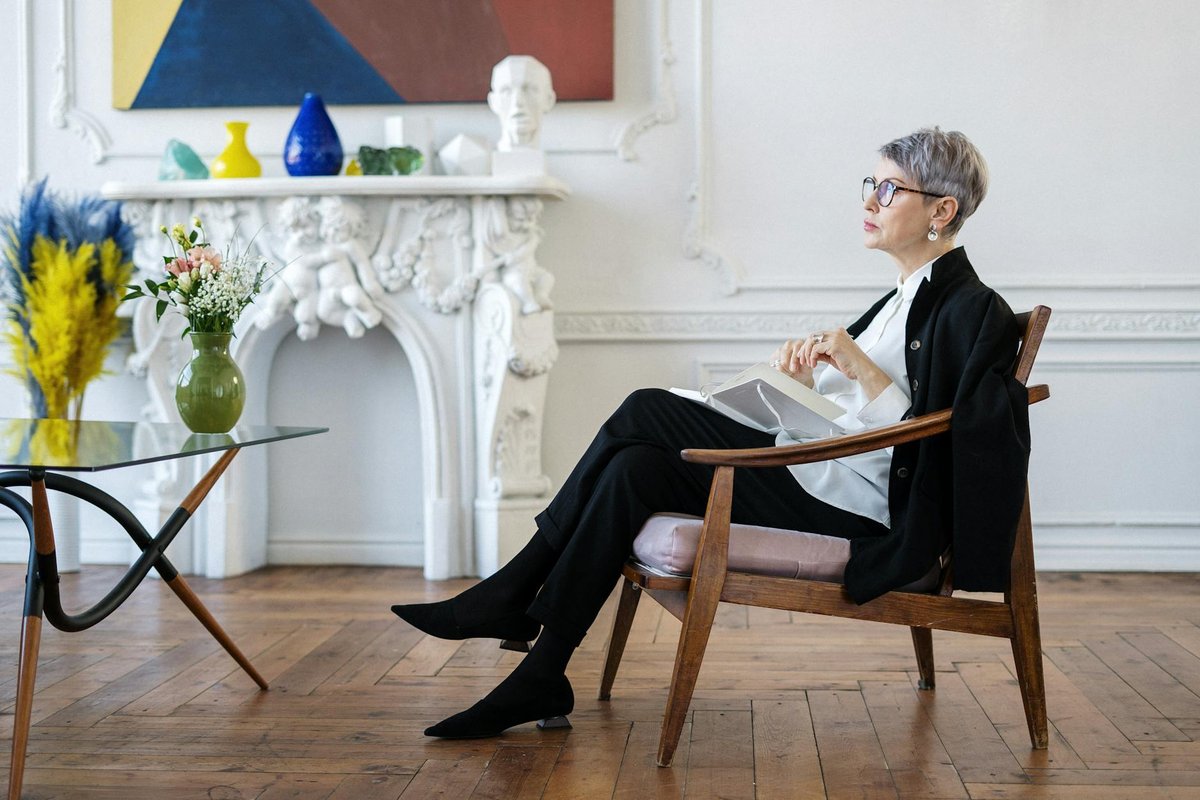 A mature woman sits pensively in a chic interior, embodying elegance and tranquility.