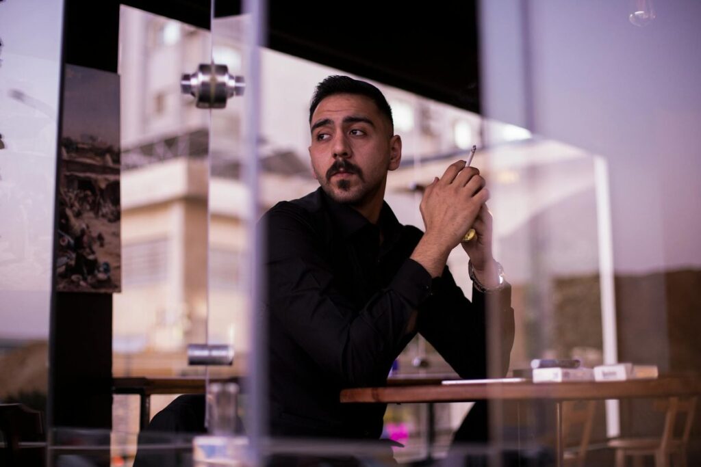 A man in a black shirt sits by a window holding a cigarette in a modern Egyptian cafe.