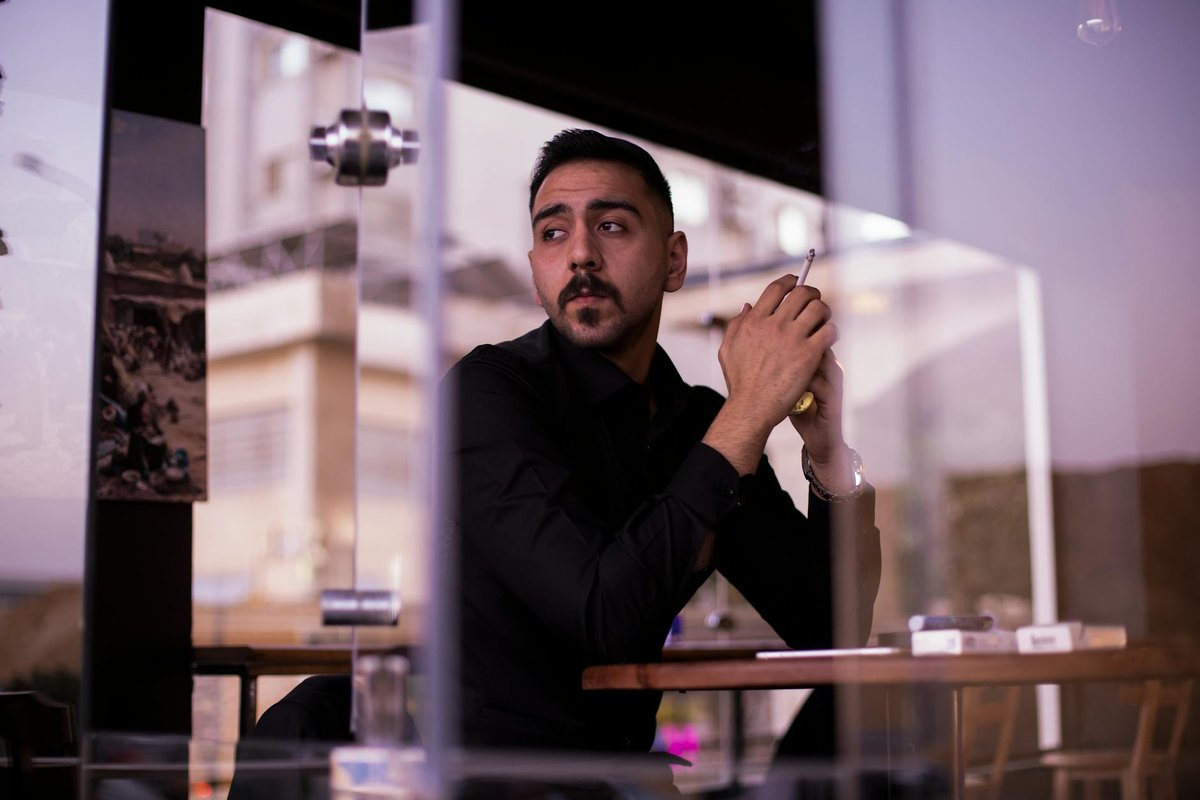 A man in a black shirt sits by a window holding a cigarette in a modern Egyptian cafe.