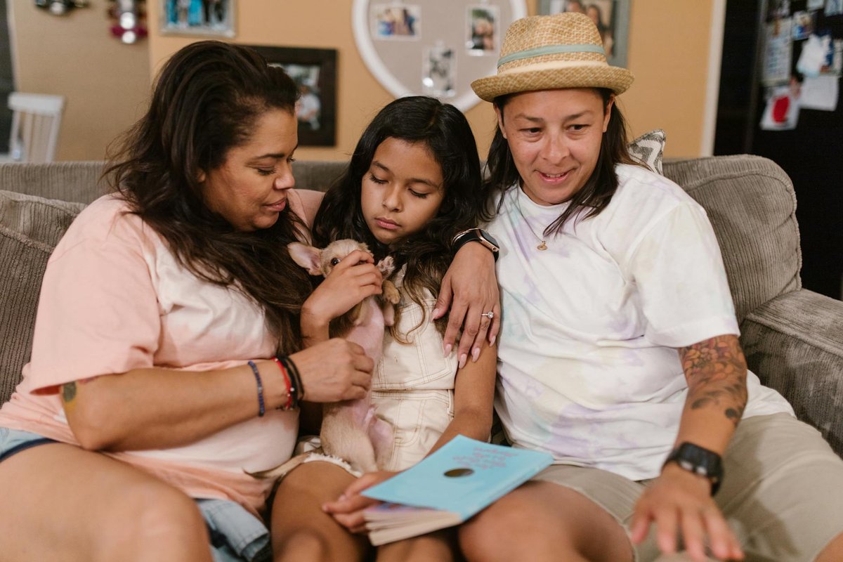 A happy same-sex couple and child relaxing indoors with a small dog, expressing love and family bond.
