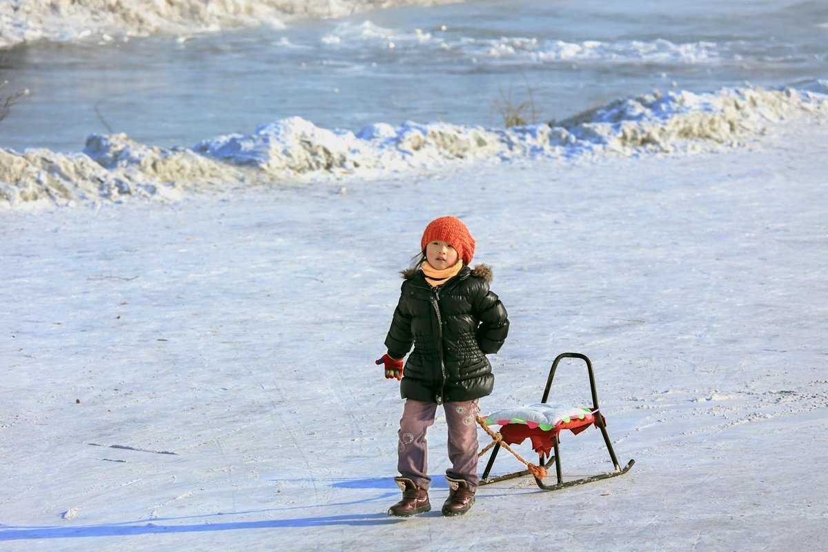 Adorable child in winter attire pulling a sled on a snowy day in Heilongjiang, China.