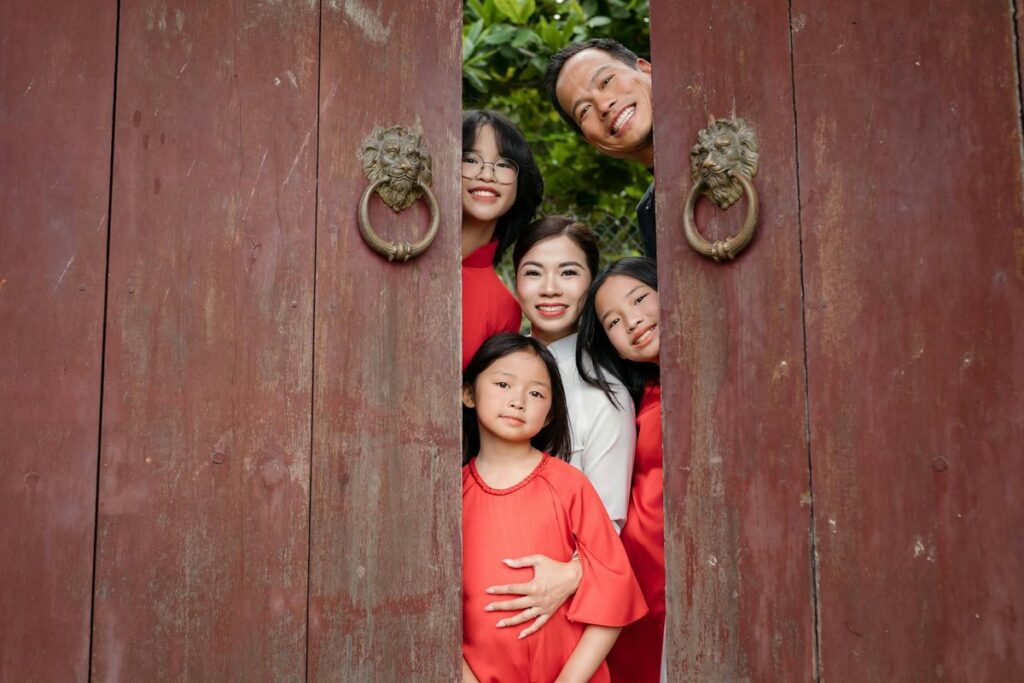 Happy family posing behind a wooden door amid greenery in Hội An, Vietnam.