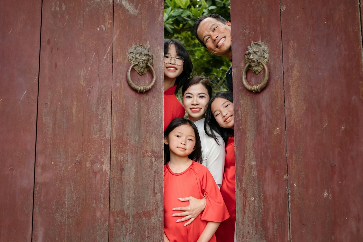 Happy family posing behind a wooden door amid greenery in Hội An, Vietnam.