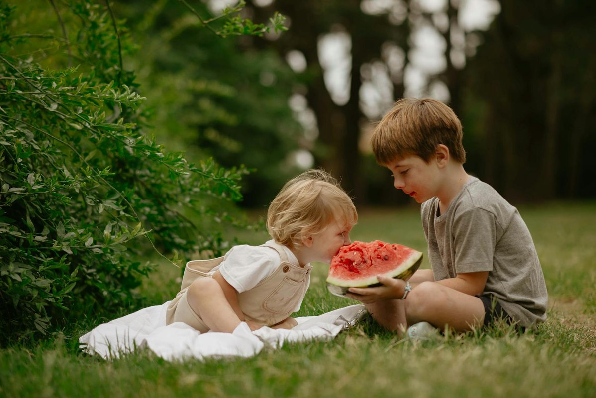 Two young children sharing a watermelon outdoors on a summer day.