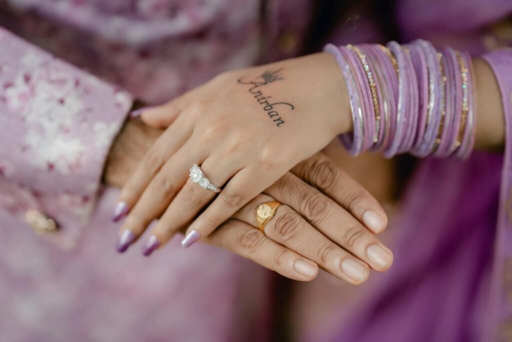 Close-up of hands showcasing wedding rings and lavender bangles, with henna tattoo. Perfect for wedding and jewelry themes.