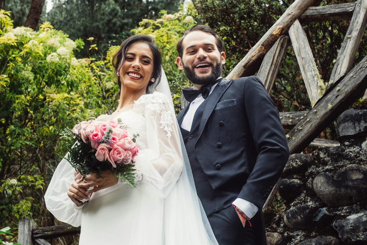 Smiling bride and groom pose outdoors, surrounded by lush greenery, capturing a joyful wedding moment.