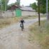 Young child riding a bicycle on a rural dirt road near village houses.