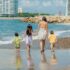 A family enjoys a sunny beach day with children playing in the sand and waves.
