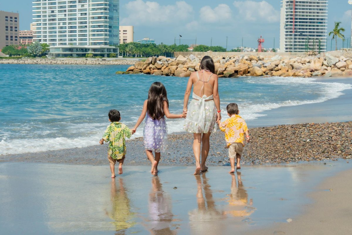 A family enjoys a sunny beach day with children playing in the sand and waves.