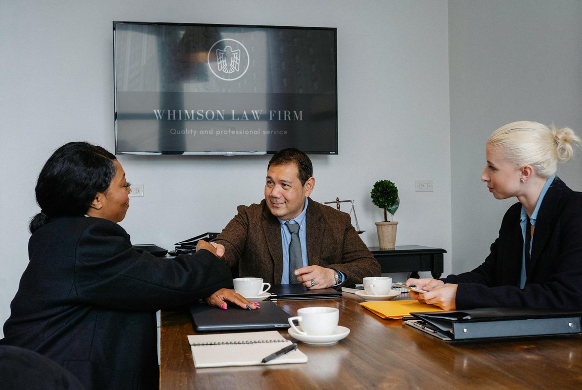 Group of multiracial coworkers in formal suits gathering at table with documents and coffee while shaking hands after verdict in court