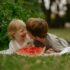 Two young children laughing and sharing a watermelon slice on a sunny summer day outdoors.