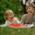 Two children smiling and enjoying watermelon on a summer day outdoors.