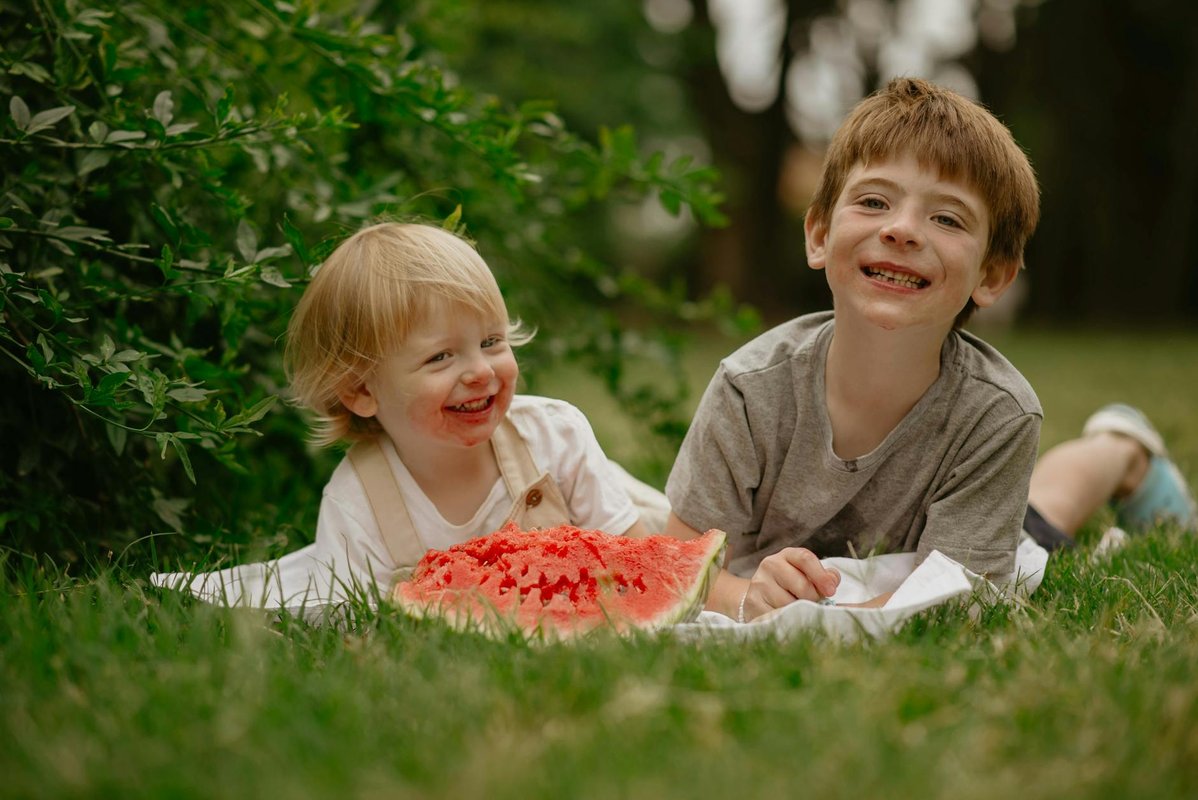 Two children smiling and enjoying watermelon on a summer day outdoors.