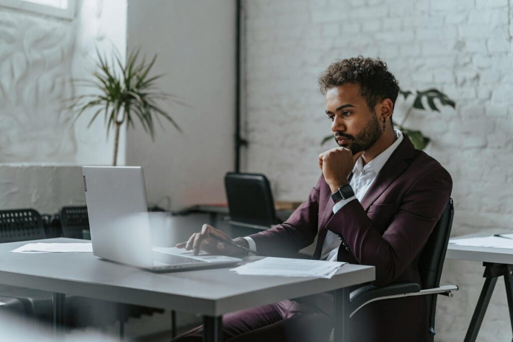 Businessman in corporate attire focused on laptop work in a modern office environment.