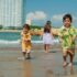 Three children enjoying a playful day at the beach with waves, sand, and sunshine.