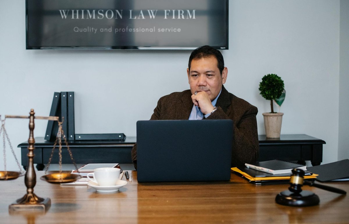Serious ethnic mature man in formal outfit working with netbook at table with gavel