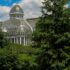 A stunning glass-domed greenhouse surrounded by lush greenery under a clear sky.