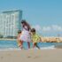 Three children playing on a sunny beach with tall buildings in the background, capturing summer joy.