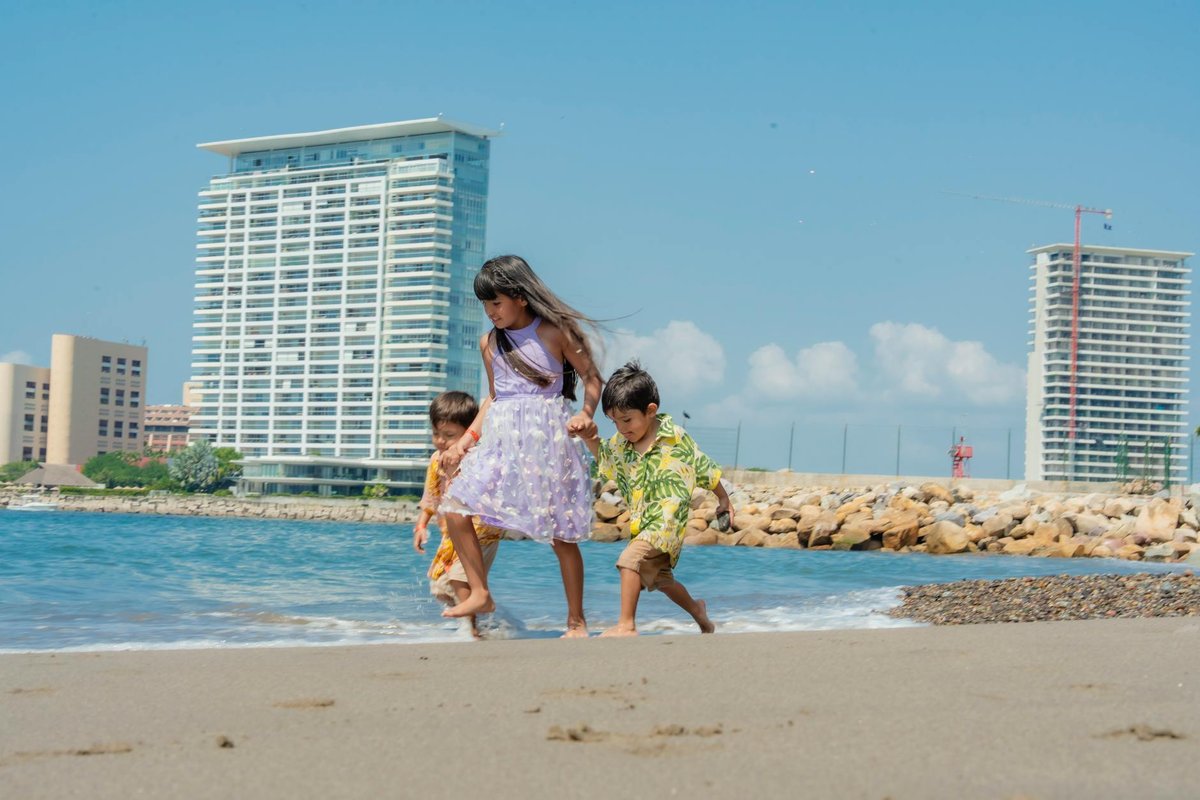 Three children playing on a sunny beach with tall buildings in the background, capturing summer joy.