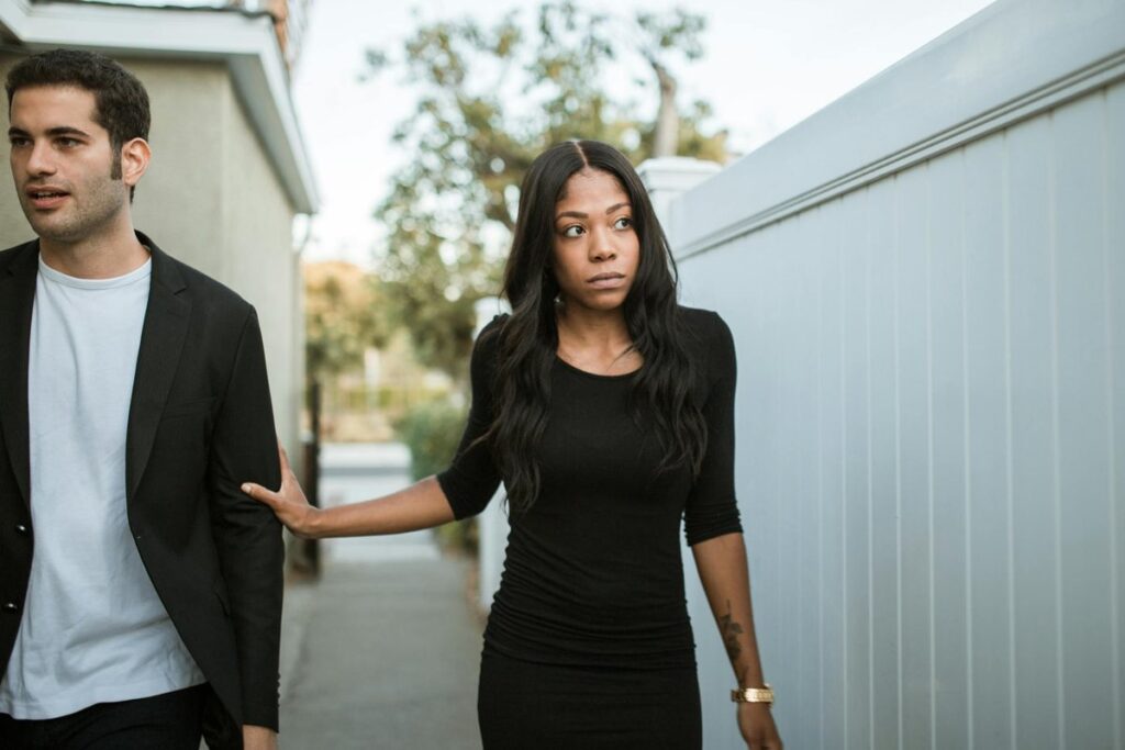 A couple walking outdoors dressed in black, showcasing serious expressions and emotional distance.