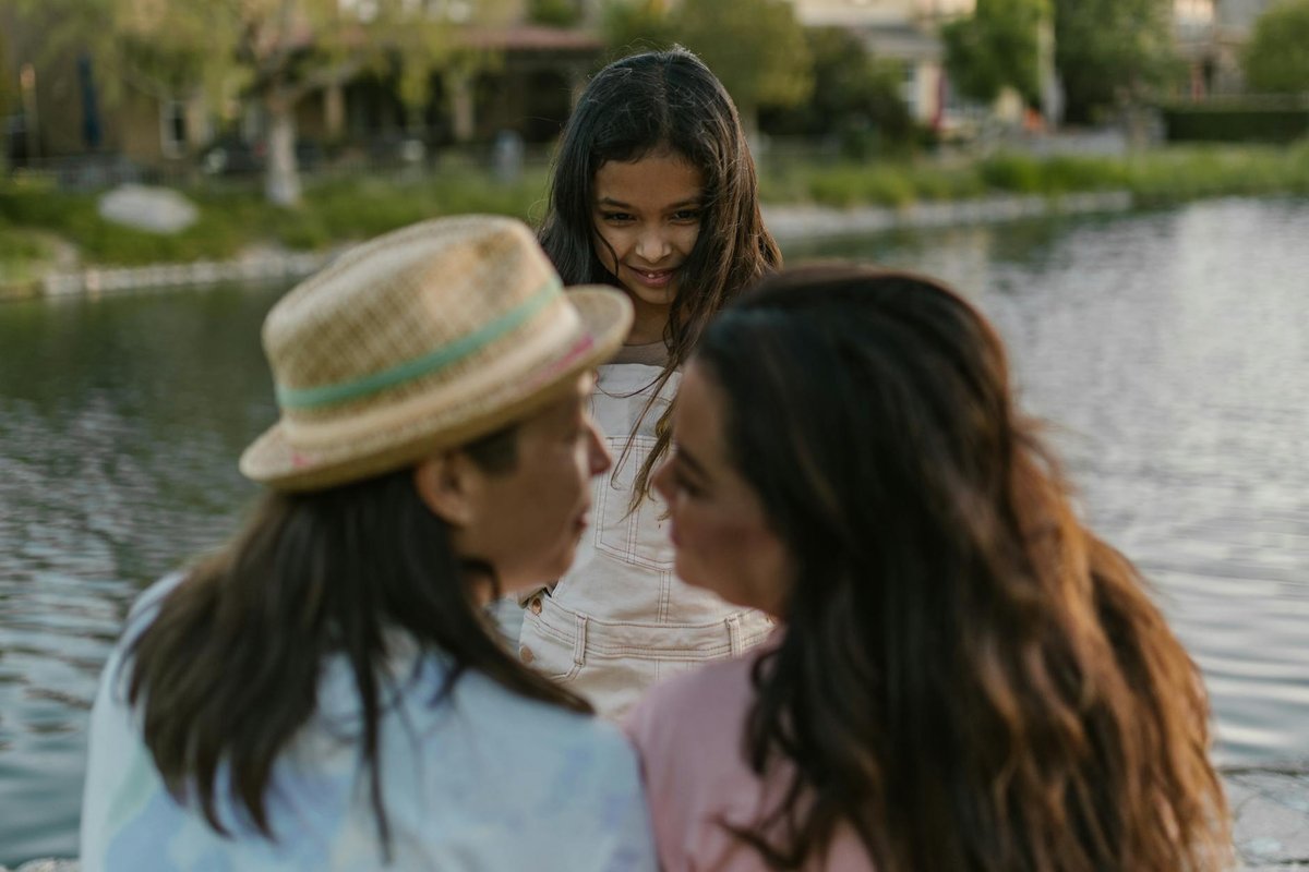 A joyful family moment by the lakeside featuring two women and a smiling child.