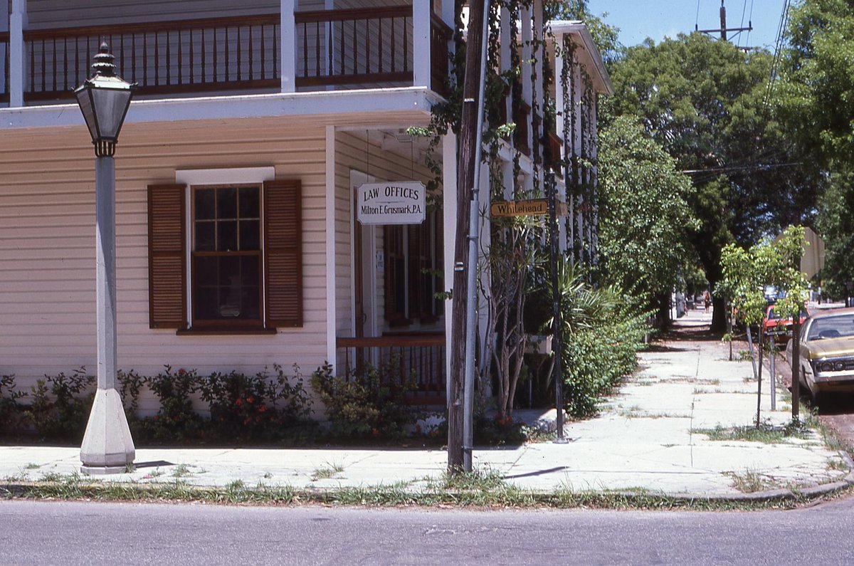 Charming historic law office with wooden shutters on a sunny corner with lush greenery.