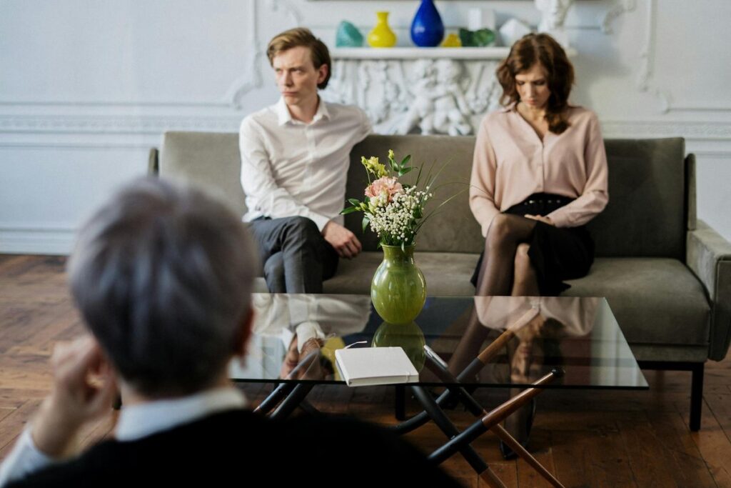 A couple sits on a sofa during a therapy session with a counselor, focusing on relationship issues.