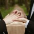 Two men in suits exchange wedding rings outdoors, symbolizing love and commitment.