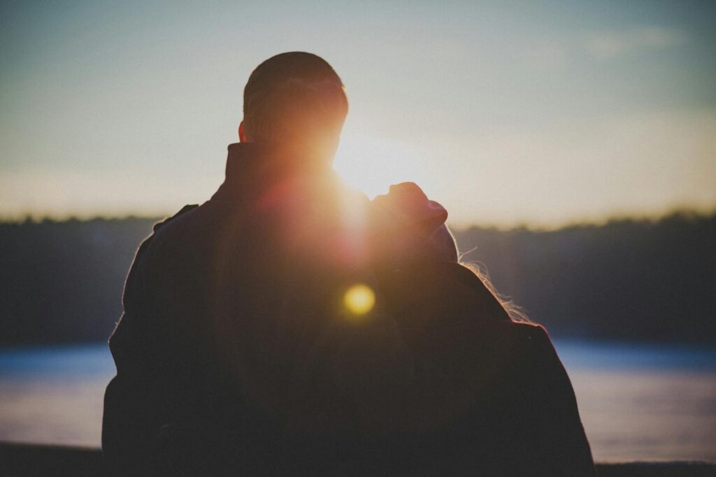 A romantic couple embraces with a beautiful lens flare at sunrise, creating a warm and intimate silhouette.