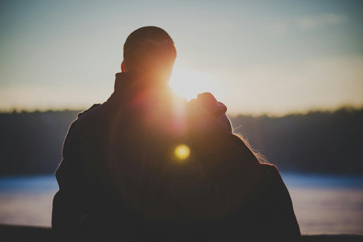 A romantic couple embraces with a beautiful lens flare at sunrise, creating a warm and intimate silhouette.