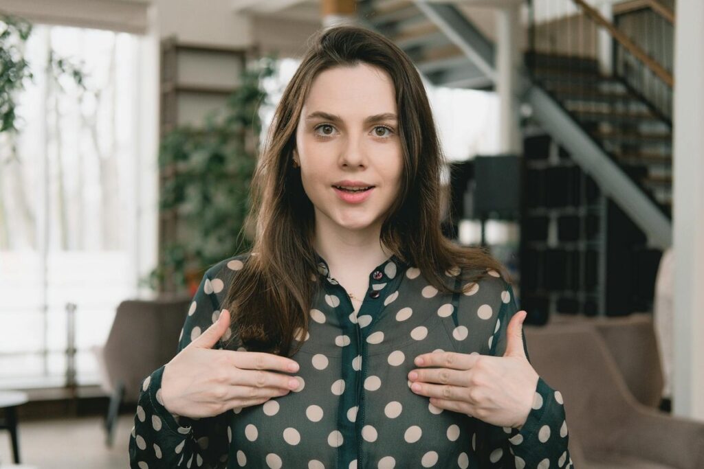 Young woman with long dark hair gesturing indoors with a smile. Ideal for content related to communication or social media.