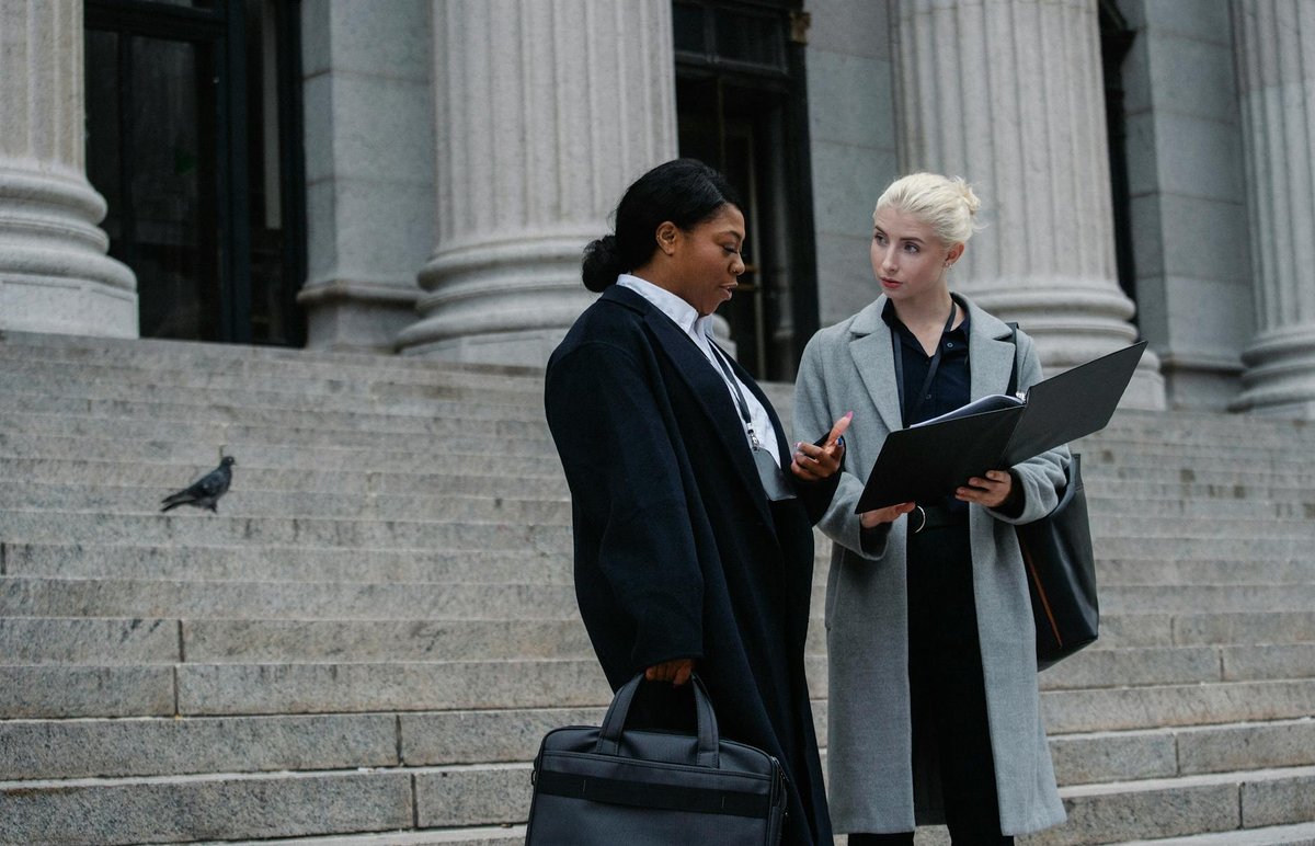 Two businesswomen discussing a document on city steps, showcasing teamwork and collaboration.