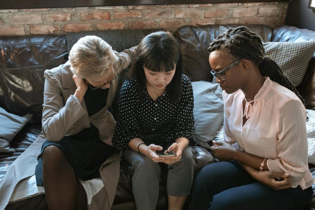 Three diverse women collaborating in a cozy office, fostering teamwork and creativity around a mobile device.