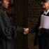 A lawyer in formal attire shakes hands with a client in a book-lined office.