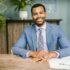 Smiling businessman in office attire sitting at a desk with documents.